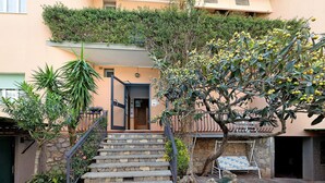 Un escalier menant à l’entrée d’un bâtiment, un petit espace extérieur aménagé avec des sièges et un arbre aux fruits jaunes.