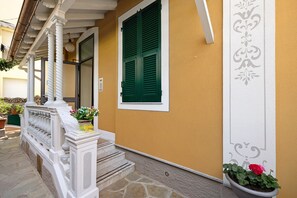 A building entrance with a white porch, green shutters, and a potted plant.