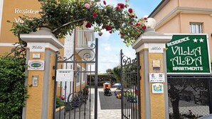 Une entrée fermée par un portail mène aux appartements de la Villa Alda, avec une enseigne indiquant le nom et une vue sur la rue.