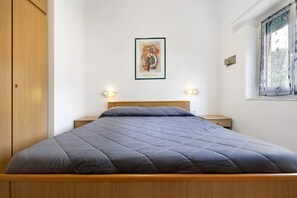 Un dormitorio con cama, armario de madera, cuadro enmarcado, lámparas de noche y ventana.