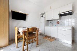 Una pequeña cocina con una mesa de comedor y sillas, un microondas, una estufa y un salpicadero de azulejos.
