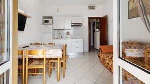 A compact kitchen with white cabinets, a microwave, and a dining area with a table and chairs. - Holiday Apartment "Numero 14" with Sea View, Balcony & Wi-Fi (Pietra Ligure)