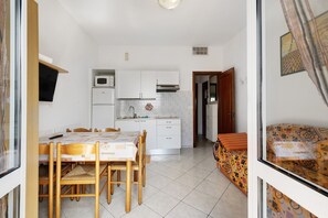 Una cocina compacta con armarios blancos, un microondas y un comedor con mesa y sillas.