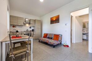 A modern kitchen with a dining table and chairs, a sofa with colorful cushions, and a painting of a sunset. - Apartment 'Casa Maria' with Lake View, Private Garden and Wi-Fi (Brenzone sul Garda)