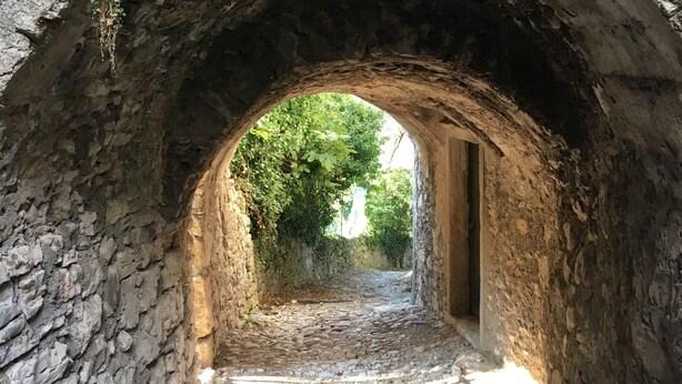 Un passage voûté en pierre, aux murs rustiques, avec un chemin pavé de pierres.
