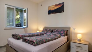 Une chambre à coucher comprenant un lit, deux tables de chevet, une fenêtre avec des rideaux et un tableau accroché au mur.