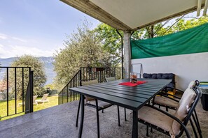 Eine Terrasse mit Tisch und Stühlen, Blick auf einen See und ein grünes Tuch.