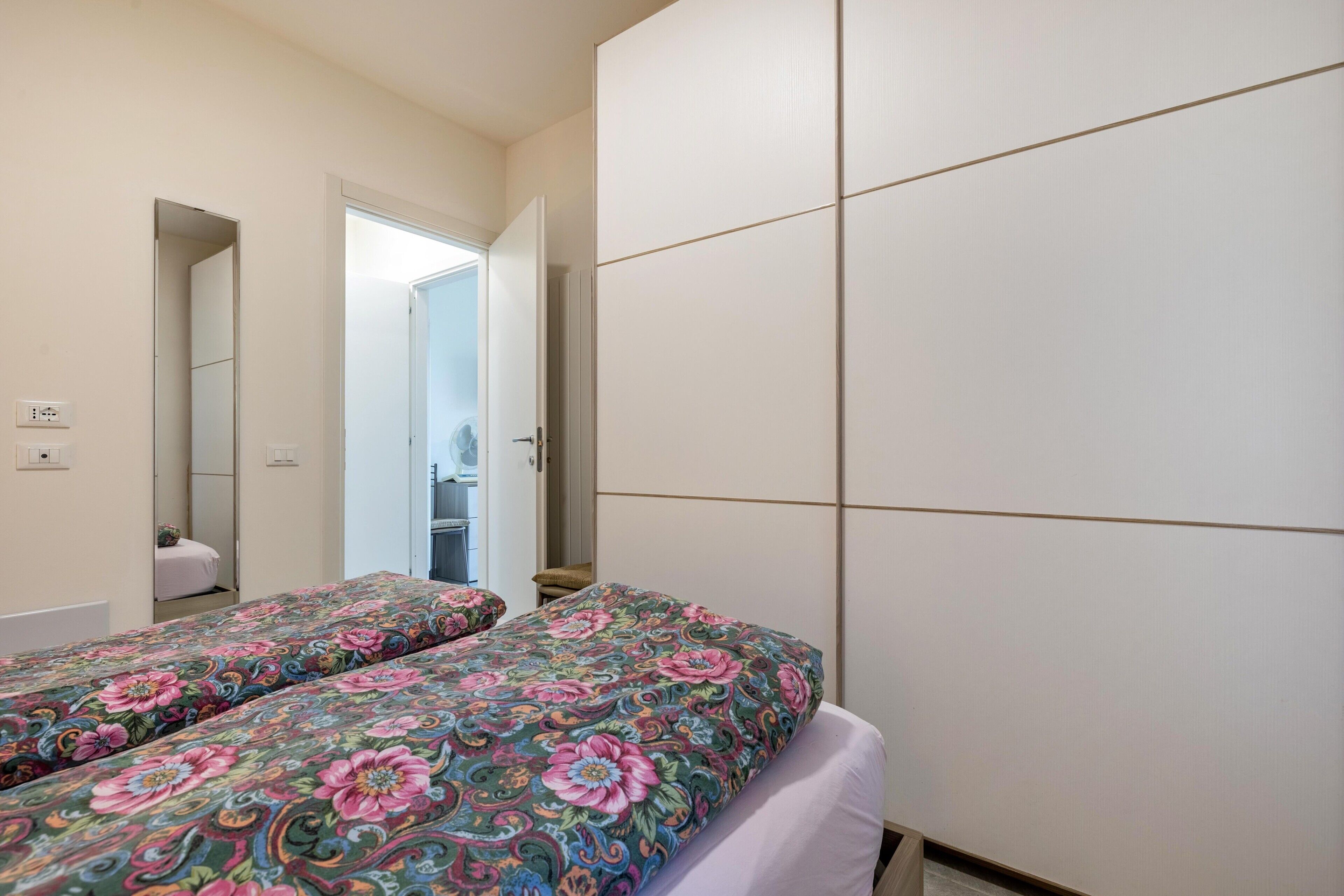 A bedroom with two beds, a wardrobe, and a mirror.