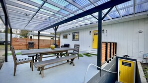 A covered patio area with a table and benches, a yellow door, and a wooden fence in the background. - Colocha’s Home – A Forest Haven (Marysville)
