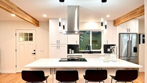 A modern kitchen with a large island, stainless steel appliances, and black bar stools. - Colocha’s Home – A Forest Haven (Marysville)