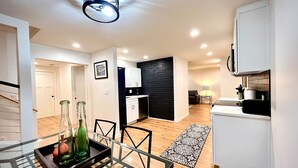 A modern kitchen with white cabinets, a black backsplash, and a dining area with a glass table and chairs. - Colocha’s Home – A Forest Haven (Marysville)