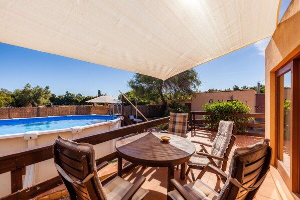 An outdoor patio with a pool, wooden chairs, a table, and a large umbrella. - Guest House 'Apartment Tina Capdepera' with Private Pool, Wi-Fi and Air Conditioning (Capdepera)