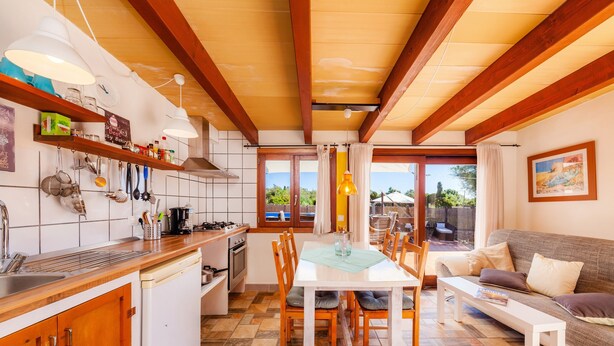 A modern kitchen with wooden beams, a dining area with a table and chairs, and a living room with a sofa. - Guest House 'Apartment Tina Capdepera' with Private Pool, Wi-Fi and Air Conditioning (Capdepera)