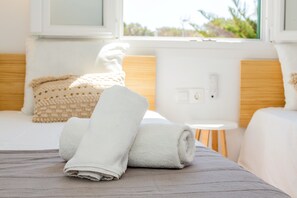 Un lit bien fait, avec une serviette blanche roulée, une petite table ronde et une fenêtre donnant sur un paysage verdoyant.