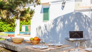 An outdoor dining setup with a stone table, plates, cutlery, glasses, and a basket of fruit. - Apartment 'Delfín 8' with Shared Pool, Wi-Fi, and Air Conditioning (Ciutadella de Menorca)