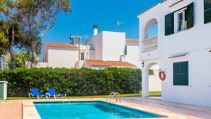 A swimming pool with lounge chairs, a white building with green shutters, and a clear blue sky. - Apartment 'Delfín 8' with Shared Pool, Wi-Fi, and Air Conditioning (Ciutadella de Menorca)