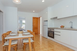 A modern kitchen with white cabinets, a built-in oven, and a dining area with wooden chairs and a table set for four.