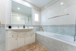 A bathroom with a large mirror, a bathtub, a sink, and cabinets.