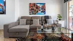 A modern living room with a sofa, a glass coffee table, and a large painting of a canal scene. - Apartment 'Cala De Mijas' with Shared Pool, Wi-Fi and Air Conditioning (La Cala de Mijas)
