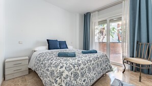 A bedroom with a bed, a chair, a nightstand, and a view of the outdoors. - Apartment 'Cala De Mijas' with Shared Pool, Wi-Fi and Air Conditioning (La Cala de Mijas)