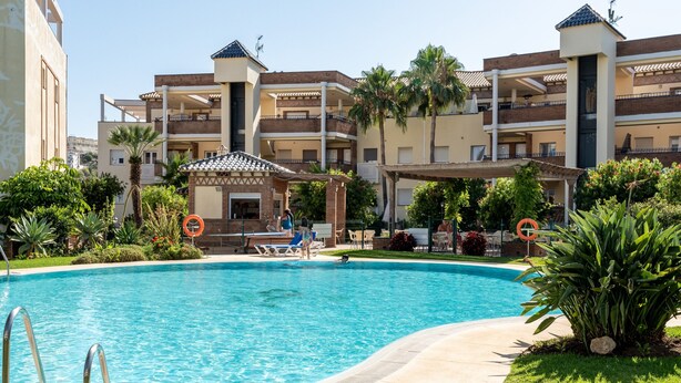 A swimming pool surrounded by a building with balconies, a covered seating area, and lush greenery. - Apartment 'Cala De Mijas' with Shared Pool, Wi-Fi and Air Conditioning (La Cala de Mijas)