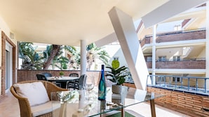 A balcony with wicker furniture, a glass table, and potted plants. - Apartment 'Cala De Mijas' with Shared Pool, Wi-Fi and Air Conditioning (La Cala de Mijas)