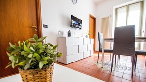 A room with a wooden door, a white console table, a TV mounted on the wall, a grey chair, and a potted plant. - Apartment 'L'Angolo di Torino' with Balcony and Wi-Fi (Torino)