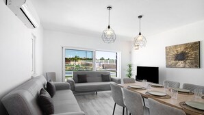 Uma sala de estar moderna com sofá, mesa de jantar, cadeiras, televisão e uma janela grande com vista.