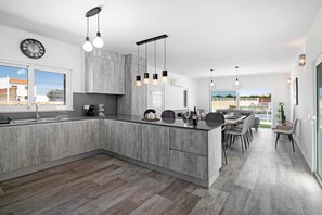 Une cuisine moderne dotée d’un grand îlot central, de luminaires suspendus et d’un coin repas offrant une vue agréable.