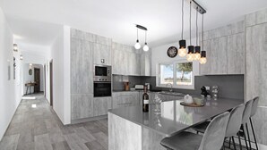 Uma cozinha moderna com ilha central, eletrodomésticos embutidos e iluminação pendente.