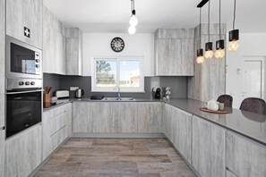 Een moderne keuken met grijze kastjes, een ingebouwde oven, een spoelbak en een klok aan de muur.