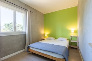 Ein Schlafzimmer mit einem Bett, zwei Nachttischlampen, einem Fenster mit Vorhängen und einer grünen Wand.