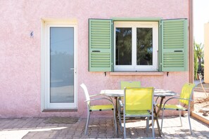 Ein pinkfarbenes Gebäude mit einer Tür, einem Fenster mit Rollläden und einem Tisch mit Stühlen.