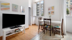A living room with a TV, wooden chairs, a dining table, and artwork on the walls.