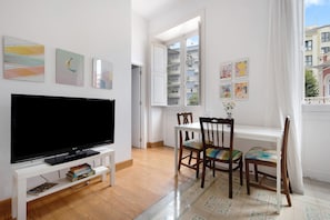 A living room with a TV, wooden chairs, a dining table, and artwork on the walls.