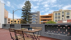 A rooftop terrace with a table and chairs, a street lamp, and buildings in the background.