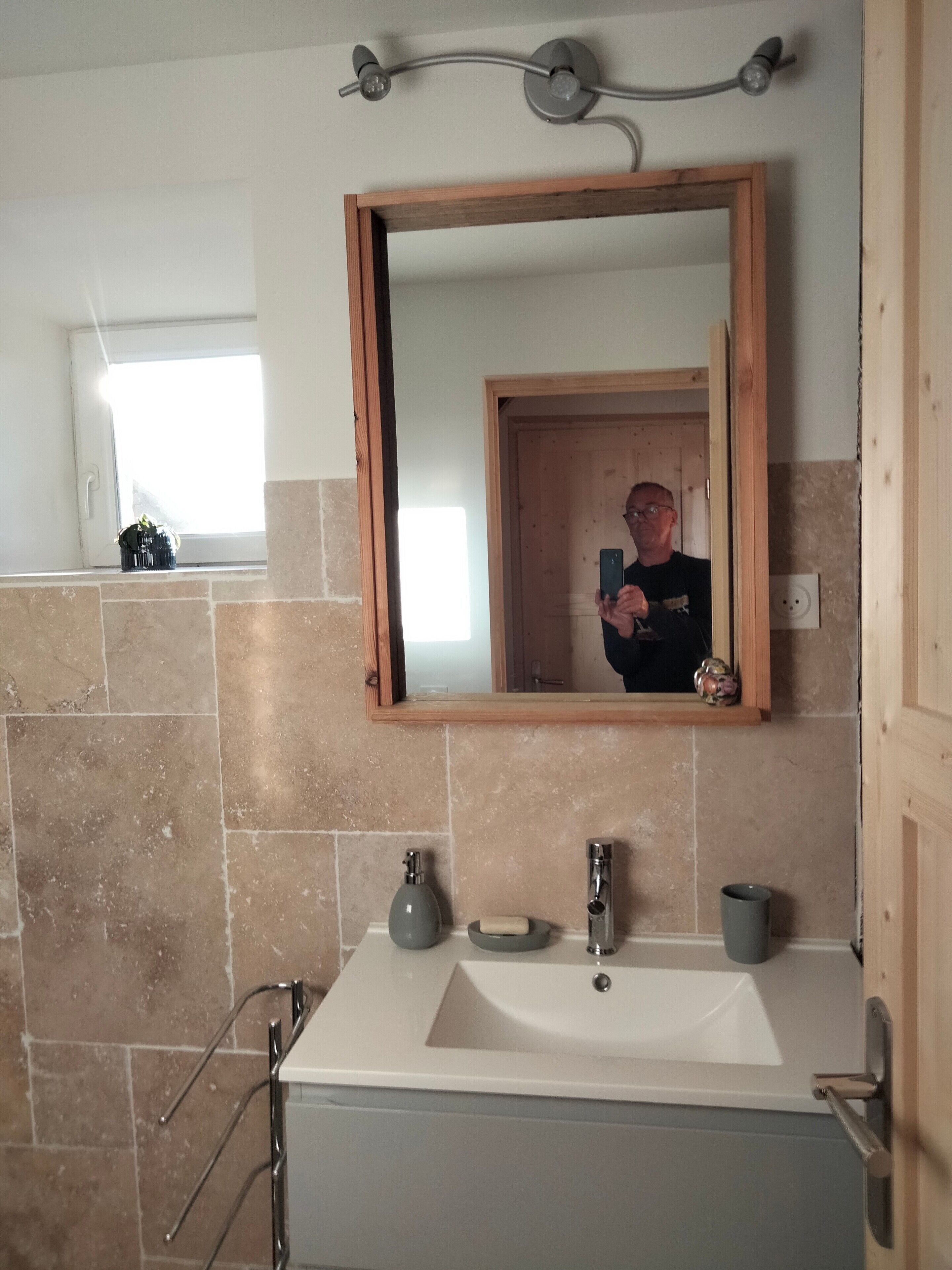 A bathroom with a large mirror, a sink, a towel rack, and a window.