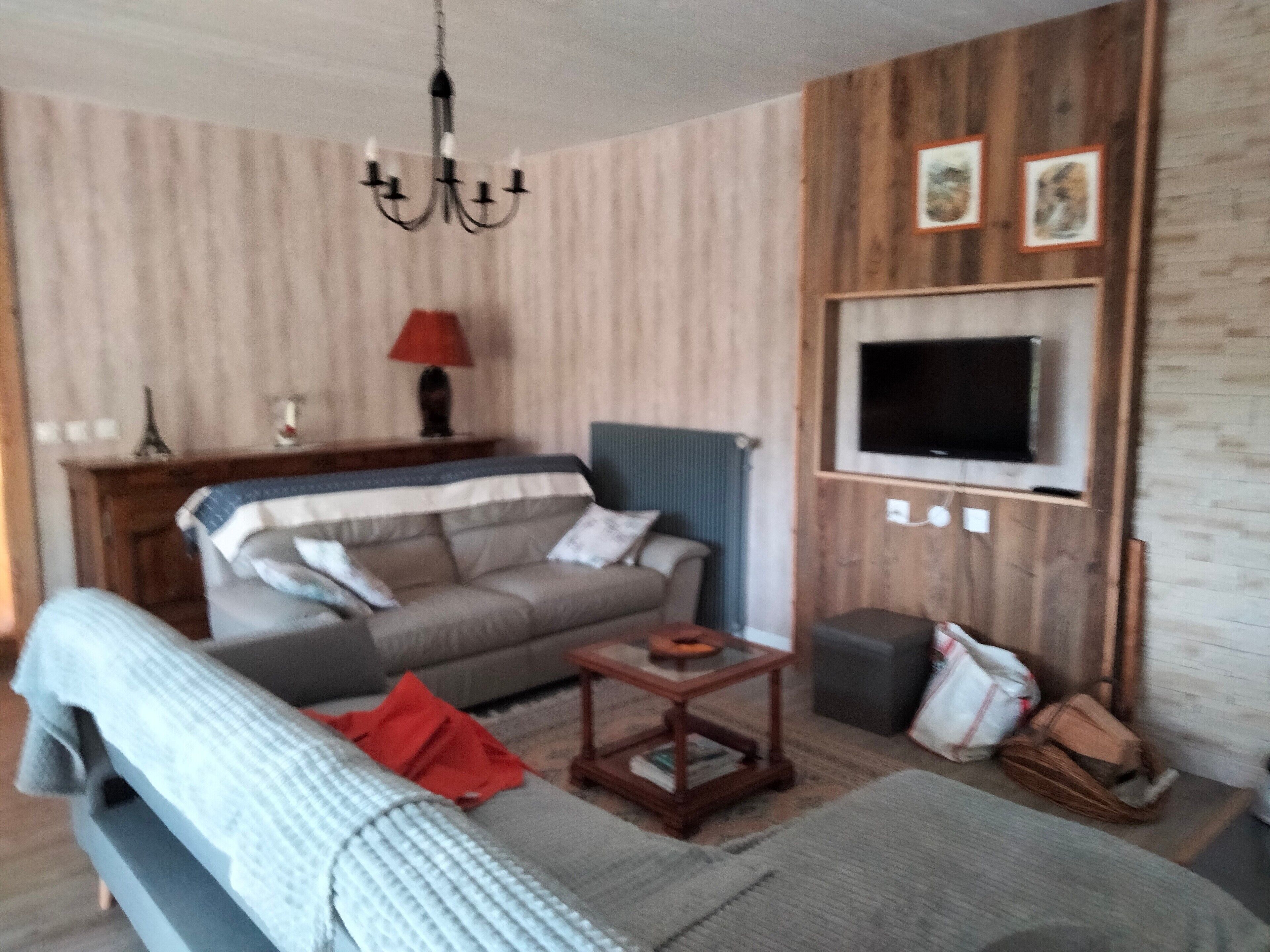 Un soggiorno con un divano, una televisione a parete, un lampadario e un tavolino.
