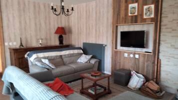 Un soggiorno con un divano, una televisione a parete, un lampadario e un tavolino.