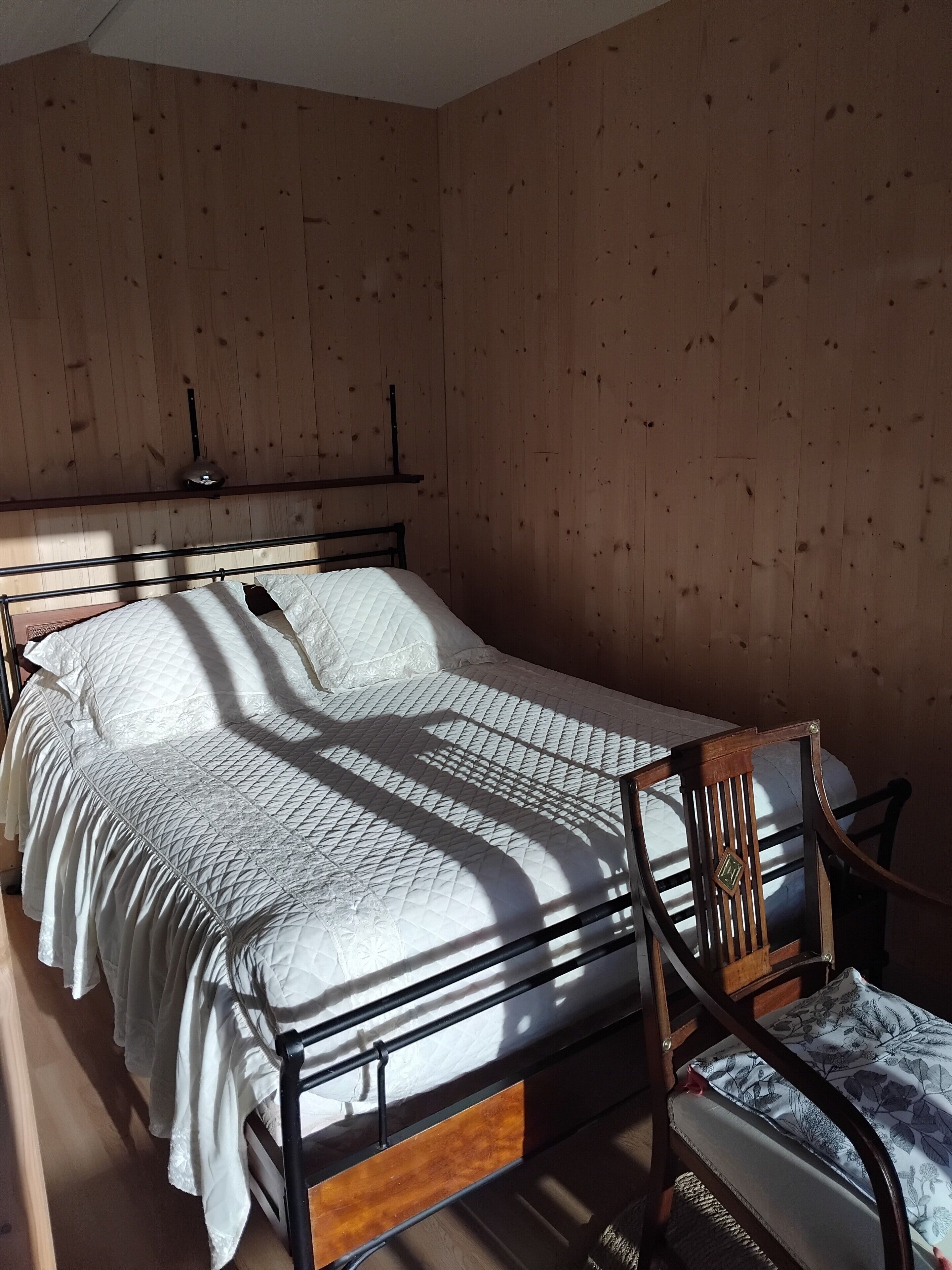 Una stanza con pannelli in legno, un letto, una sedia e una mensola.