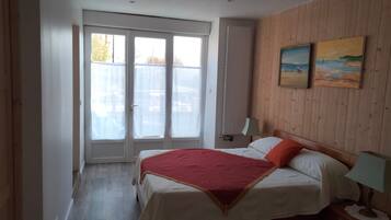 A bedroom with a bed, a nightstand, a lamp, a window with blinds, and a painting on the wall.