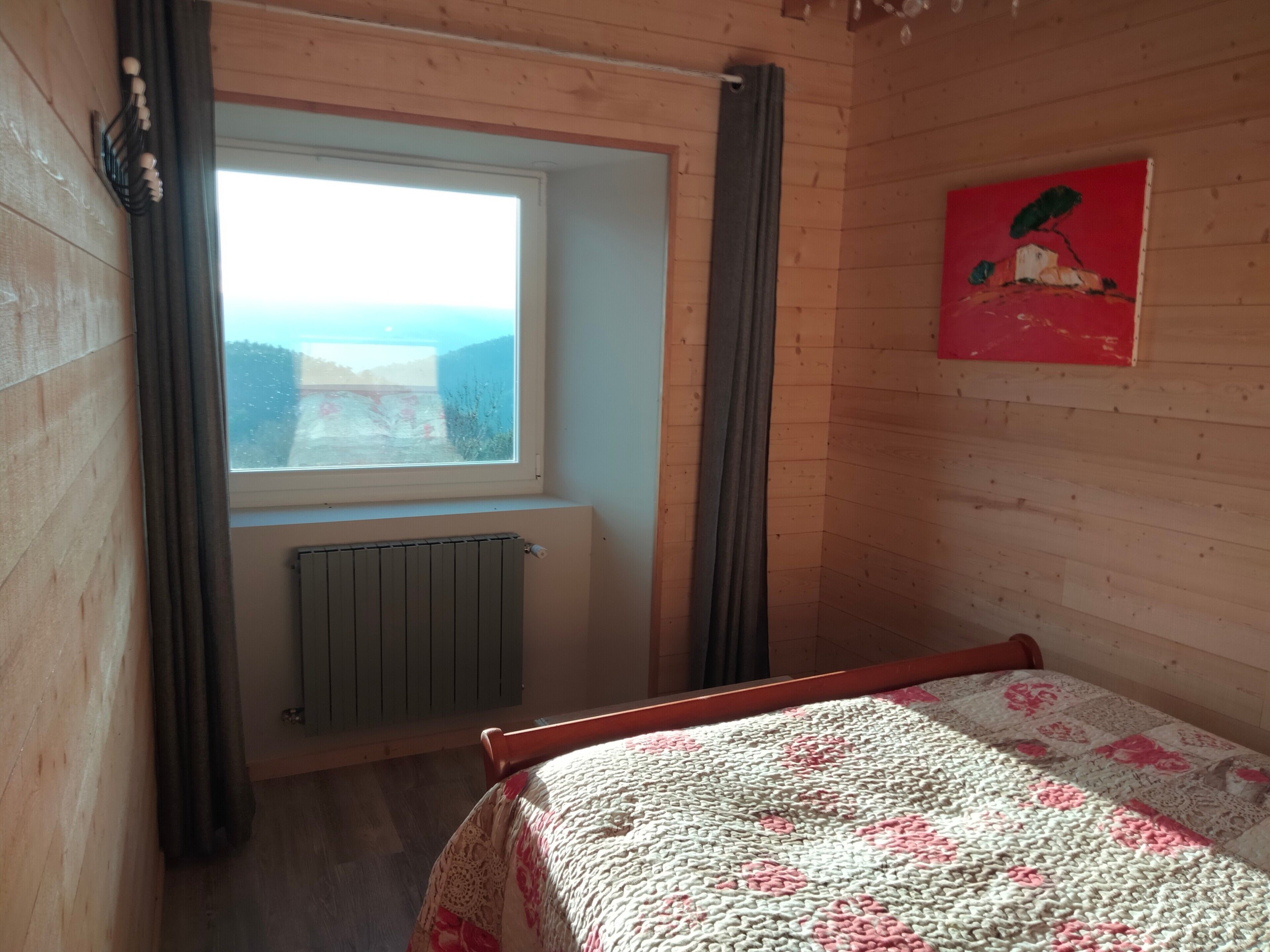 A room with a bed, a window, a radiator, and a painting on the wall.