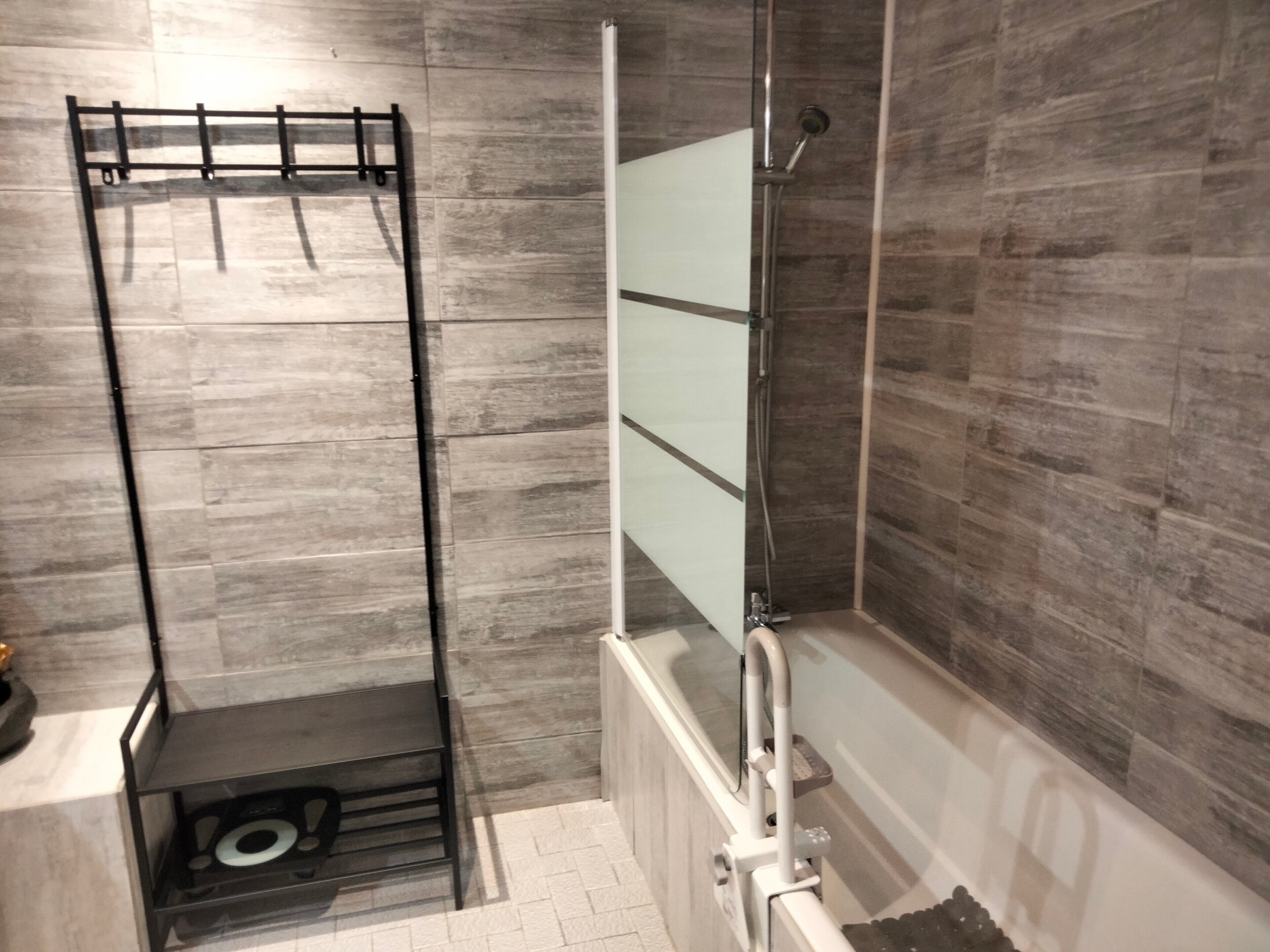 A shower area with a glass enclosure, a metal rack, and a tiled floor.