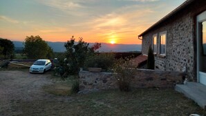 A house with a stone exterior, a car parked in the driveway, and a sunset in the background.