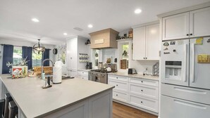 Een moderne keuken met witte kasten, een centraal eiland, een kookplaat en een koelkast.