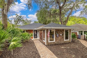 A two-story building with a brick facade, a front porch, and a small garden area with palm plants.