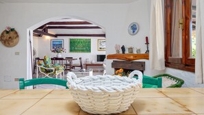 Un comedor con una mesa, sillas, una cesta decorativa y vistas a otra habitación con un cuadro y una ventana.
