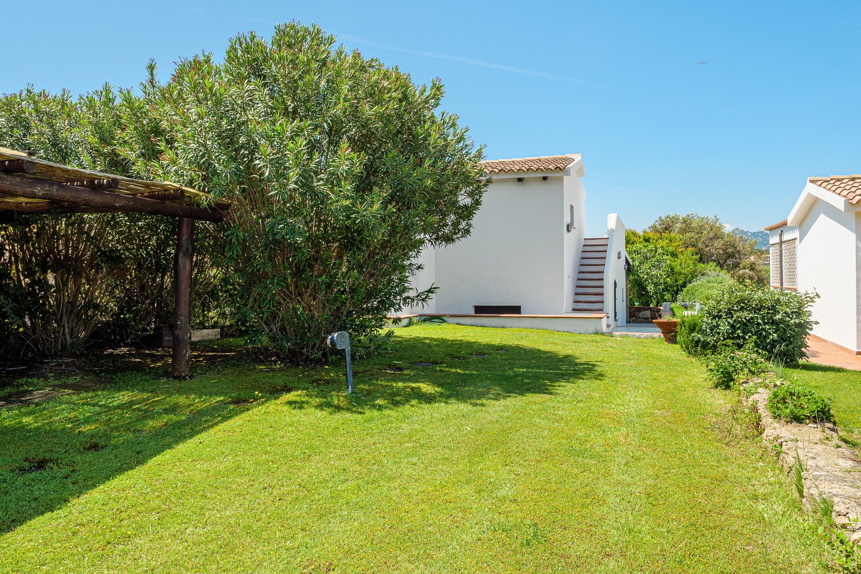 Un bâtiment blanc avec un toit en tuiles, une pergola en bois et une pelouse bien entretenue.