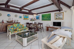 Uma sala de estar com sofá, mesa de centro, TV, mesa de jantar, cadeiras, obras de arte e um modelo de navio.