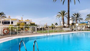 A swimming pool with a white fence, palm trees, and a building with yellow accents in the background.